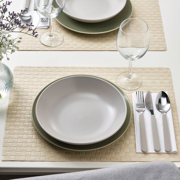 Table setting with FÄRGKLAR deep plates in neutral shades. Includes wine glasses, silverware, and woven placemats.