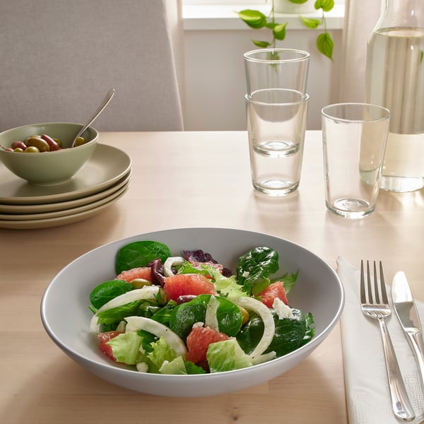 Table set with FÄRGKLAR dish, containing salad. Two glasses, utensils, bowl with olives also visible.