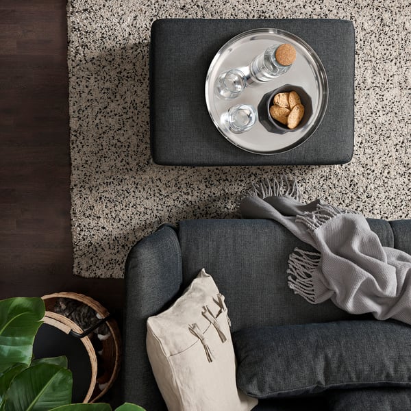 Modern living room: grey FAMMARP sofa, grey throw, circular tray with cookies and glasses on patterned rug, beside plants & basket.