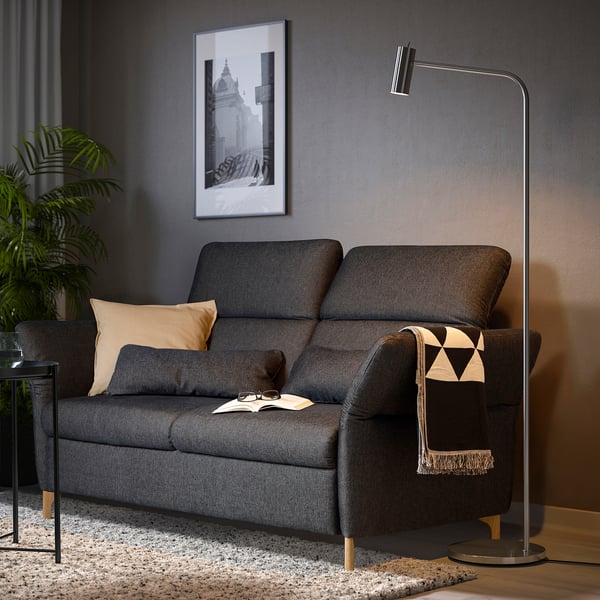 Modern living room with grey FAMMARP sofa, black and white throw, tall floor lamp, beige pillows, and black picture frame on dark wall.