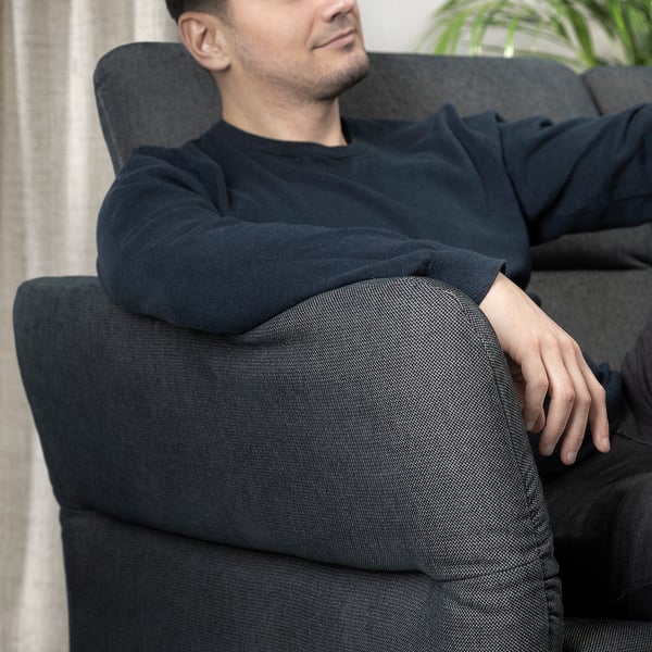 Person reclines on black FAMMARP sofa, armrests adjusted, dark chenille cover, cosy living room setting.