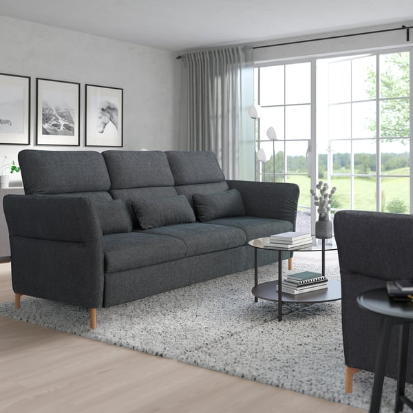 Modern living room with large dark grey FAMMARP sofa, sleek coffee table, grey rug. Sofa dominates, curtains frame large window.