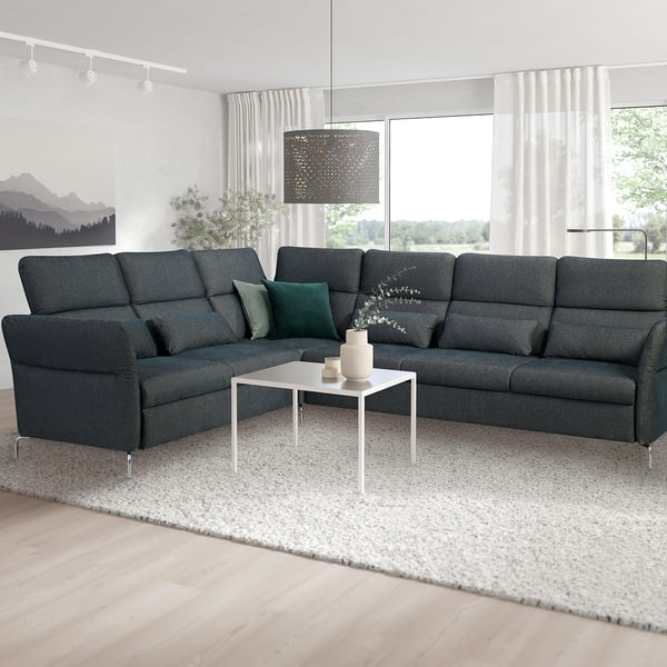Modern living room with large grey FAMMARP l-shaped sofa, dark green pillows, white coffee table, large window, and abstract rug.
