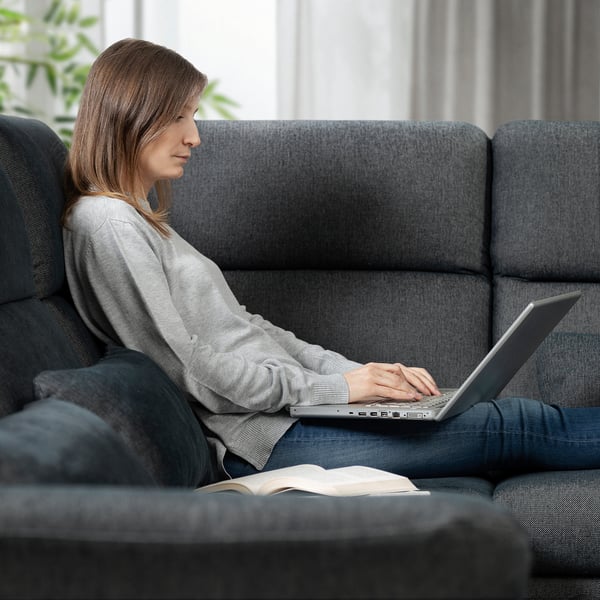 A person sits on a grey FAMMARP sofa, using a laptop while an open book rests beside the person.