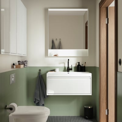 Modern FAXÄLVEN mirror in bathroom with subtle light frame, green tiles, grey towel, black tap, white basin.