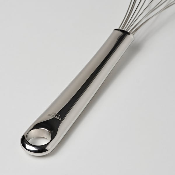Stainless steel whisk with polished, ergonomic handle and hanging hole, lying on a clean surface.