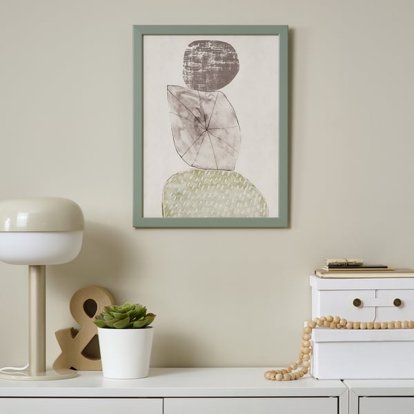 Framed abstract art hangs on a beige wall above a white cabinet. A white lamp and small potted plant sit on the cabinet.