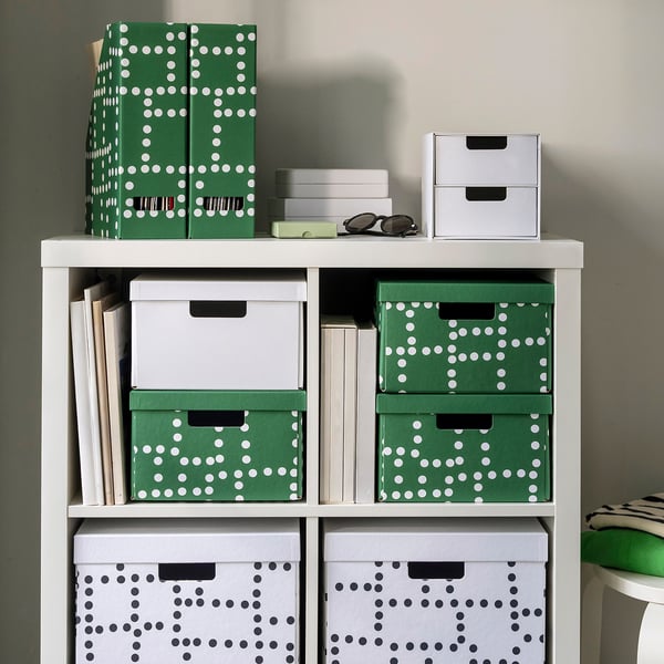 White shelf with green and white polka dot boxes, holding books, papers, and sunglasses.