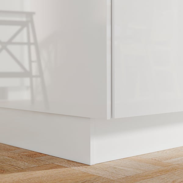 A white FÖRBÄTTRA kitchen plinth. It is sleek, glossy, and sits flush against the wooden floor.