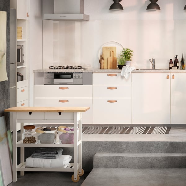 Modern kitchen with white cabinetry, black countertop and stainless steel appliances. Central island on wheels made of birch wood.
