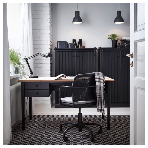 Modern home office with black FORSÅ desk lamp, black chair, dark patterned rug, and black cabinet with a potted plant and espresso machine.