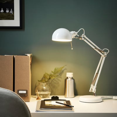 White desk lamp with adjustable arm on white desk, light focused among plant, water bottle, files.