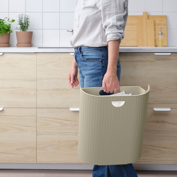 Person holding a GÅRDSBUTIK bin, used for waste sorting. The bin has an integrated handle for easy lifting and can be mounted on walls.