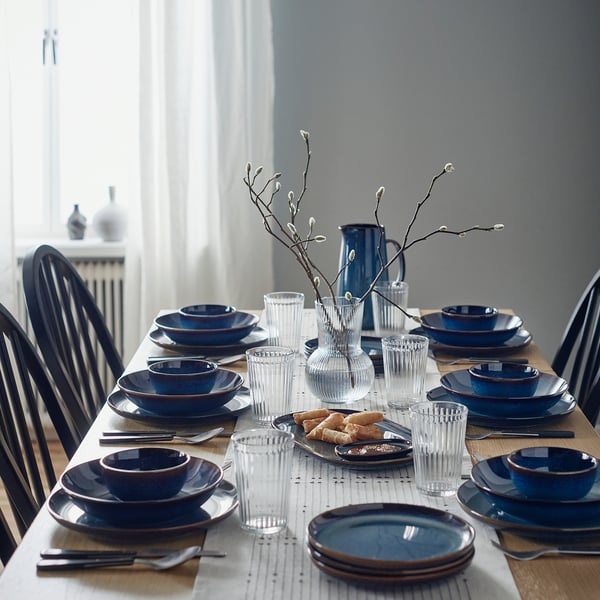 Blue stoneware table setting with plates, glasses, cutlery, and decorative branches.