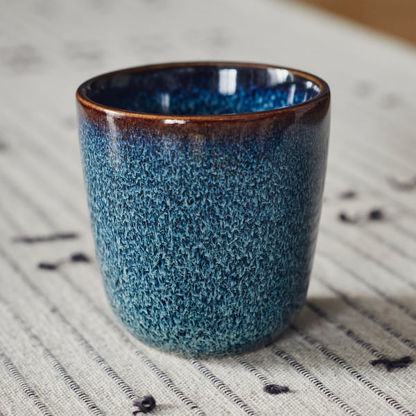 Crafted stoneware cup with deep blue glaze and brown rim, resting on a textured cloth.