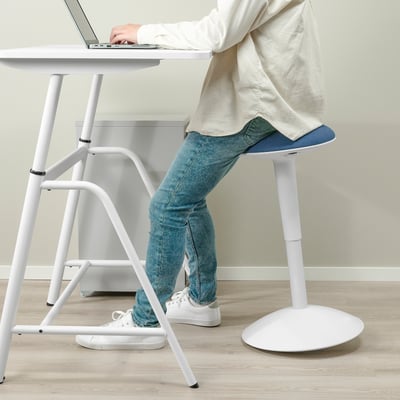Person using white sit/stand desk, typing on laptop while sitting on high stool with blue seat.