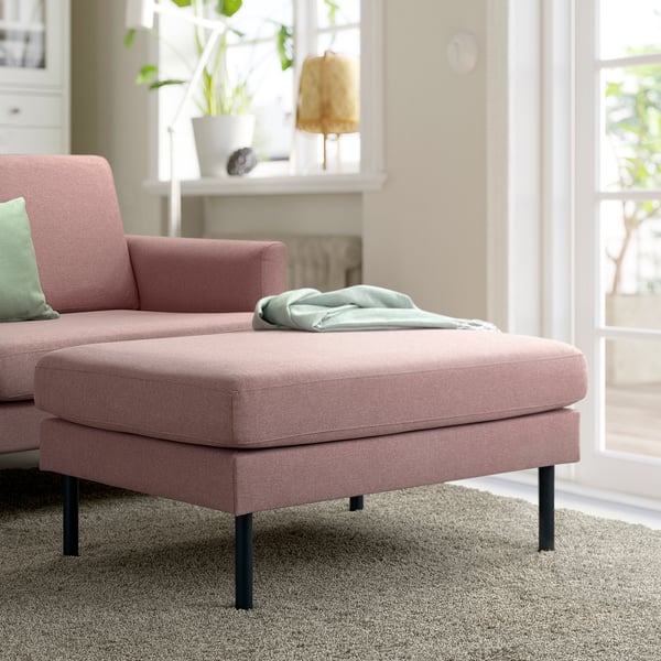 Modern pink fabric sofa with cushions, light grey throw, cosy decor, and large window.