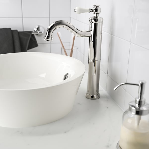 Modern chrome faucet, ceramic handles, atop large white basin sink with soap dispenser.