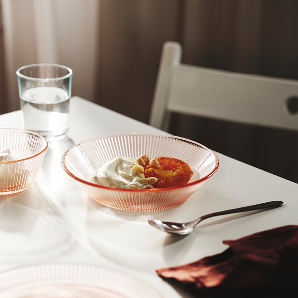 A small glass serving bowl with a red rim holds dessert, beside a spoon and glass on a table.