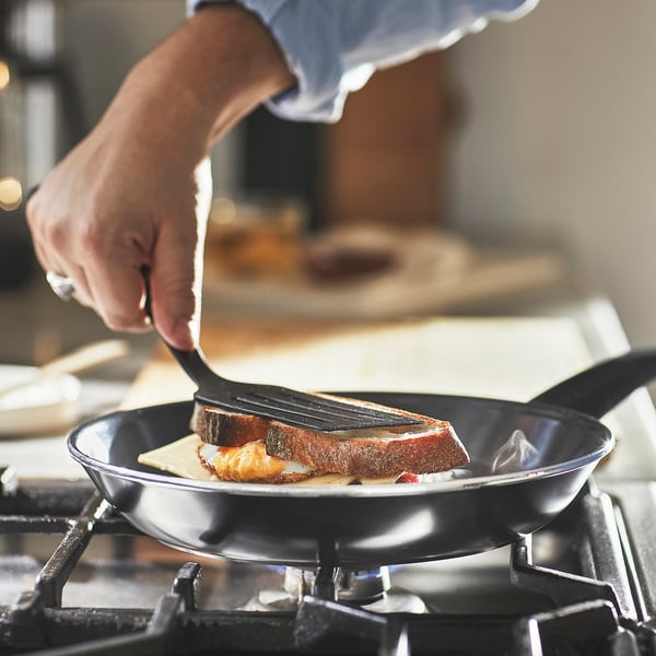 Person flips grilled cheese sandwich in black non-stick skillet on stovetop.