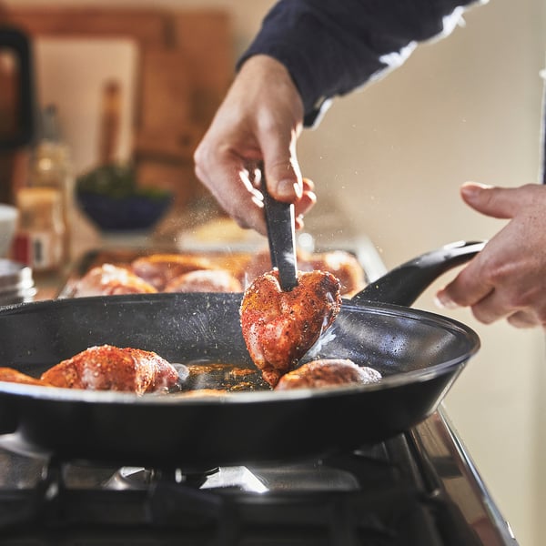 Person cooking chicken in a large, non-stick frying pan on a stove. Handles ensure easy lifting.
