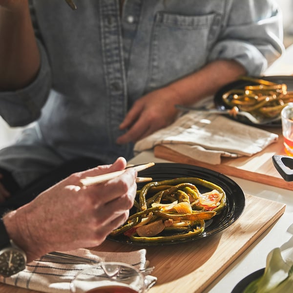 A person is cooking vibrant vegetables in a deep wok with a glass lid, showcasing even heat distribution and easy monitoring.