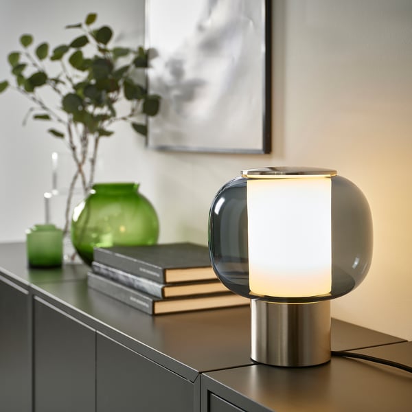 HÖGVIND lamp in smoked glass on table, with green vases & books.