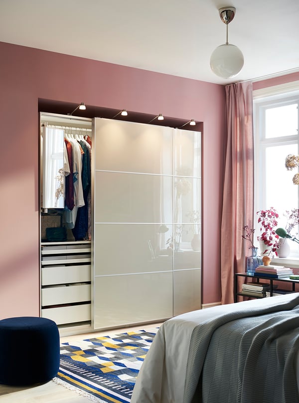 Modern bedroom a large HOKKSUND high-gloss white sliding closet, pale pink walls, instagram-worthy decor with grey bed, and a patterned rug.