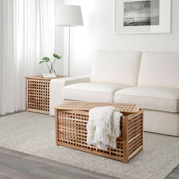 Cosy living room scene: cream sofa, wooden lattice side table with blanket, rug, and plant.