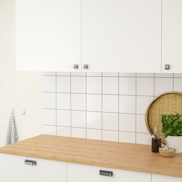 A modern kitchen with a wooden countertop, white tiled backsplash, hanging towels, and potted herbs, demonstrating a functional and organised space.