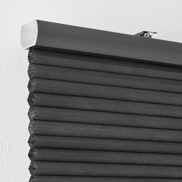 Grey cellular window blind closes for room darkening and privacy, mounted on wall.