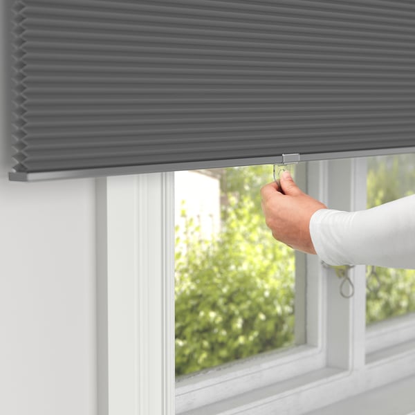 Person adjusts grey cellular blind on window. The blind darkens room, insulates air, and provides privacy.