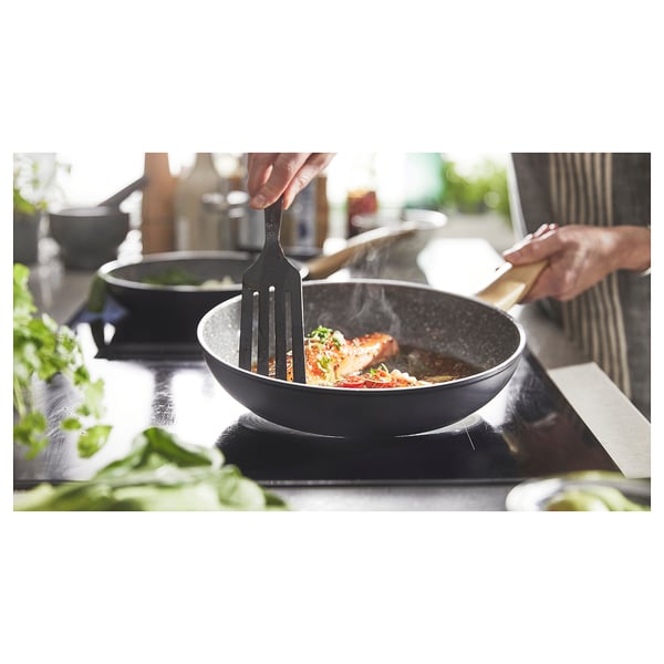 Chef cooking fish in HUSKNUT pan on stovetop.