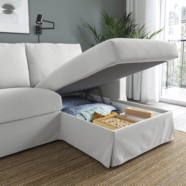 White sectional sofa with lift-up chaise, revealing storage filled with blankets and games.