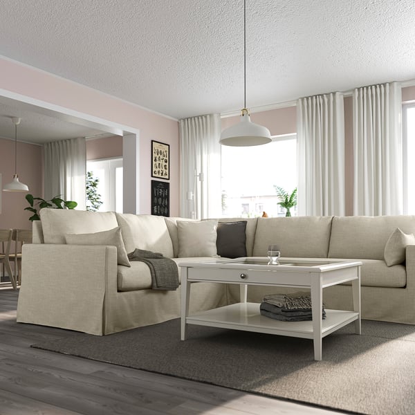 Modern living room with beige HYLTARP sectional, coffee table, grey pillows, wooden floor, large windows.
