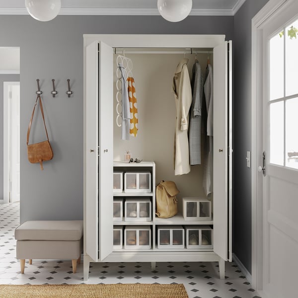 Modern white wardrobe with bifold doors, hanging clothes, shelves, and storage boxes.