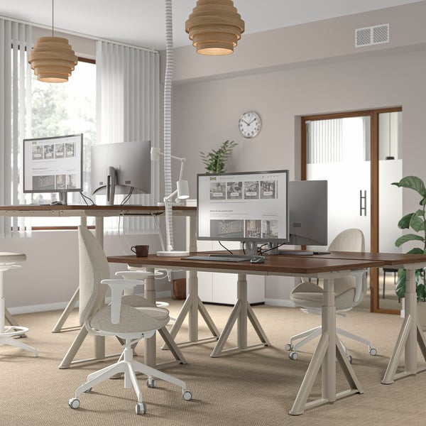 Modern office with IDÅSEN desks, chairs, monitors, lights, clock, window, plant.
