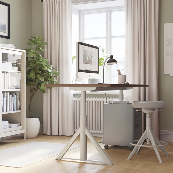Modern adjustable IDÅSEN office desk with computer, plant, and bookshelf.