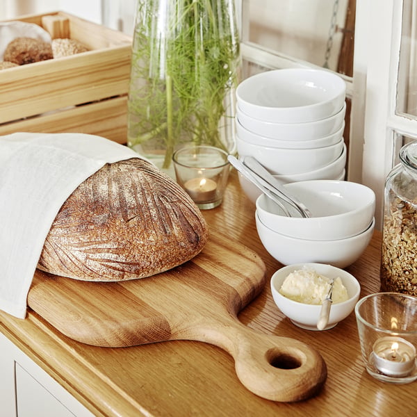 Breakfast scene with rustic bread, bowls, and candles on wooden surfaces.