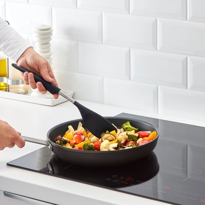 Cooking colourful veggies in frying pan with spatula, induction stove.