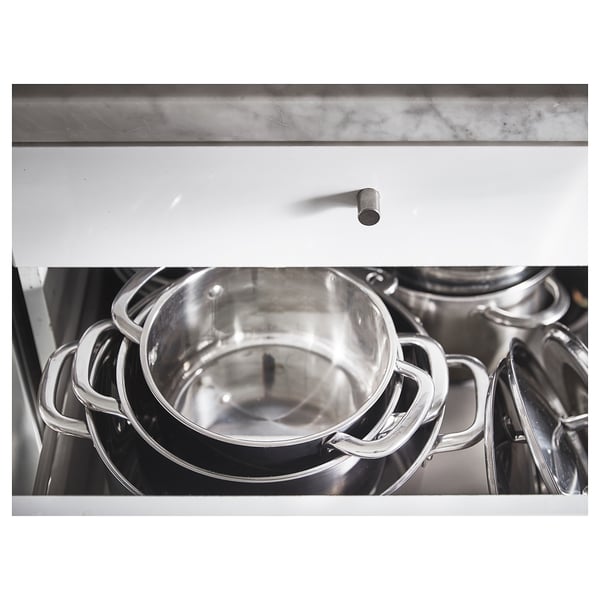 Black and white stacked stainless steel pots, with one handle visible. The pots are stored in a white cabinet.