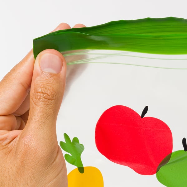 Hand holding a fresh green leaf, with 3d renderings of colourful fruits and vegetables in the background.