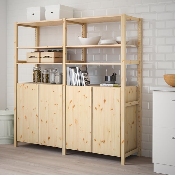 Wooden IVAR storage unit with shelves and items, beside white brick wall.