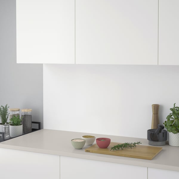 Modern kitchen counter with white cabinets and backsplash. Wooden cutting board with bowls and herbs. Spices, grinders, plants.