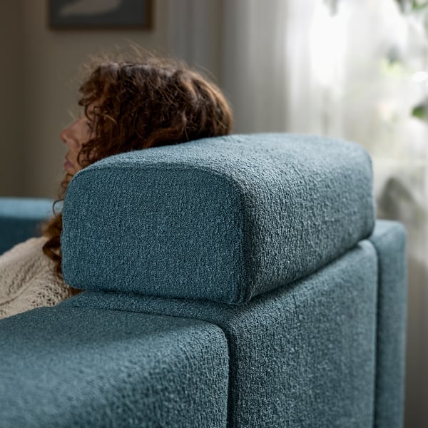 A person rests on a cushioned, grey JÄTTEBO sofa, using the removable headrest pillow for support.