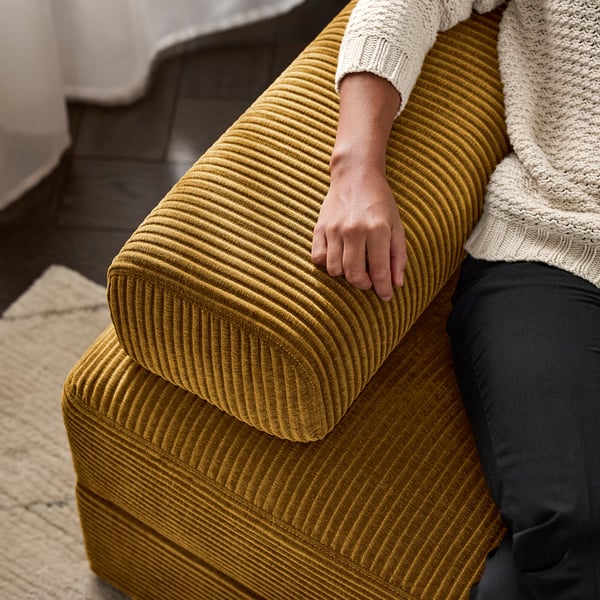 Person sitting on yellow corduroy JÄTTEBO modular sofa, resting hand on armrest.