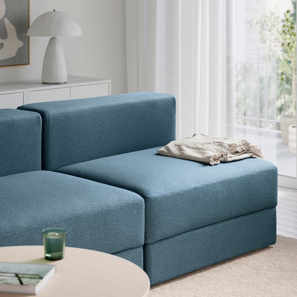 A blue sectional sofa with a beige blanket. It has storage under the seat.