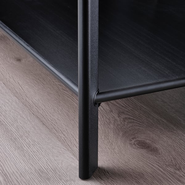 Close-up of a sleek, black table leg with a shiny, rounded finish. Modern design with smooth, metallic detailing on wooden floor.