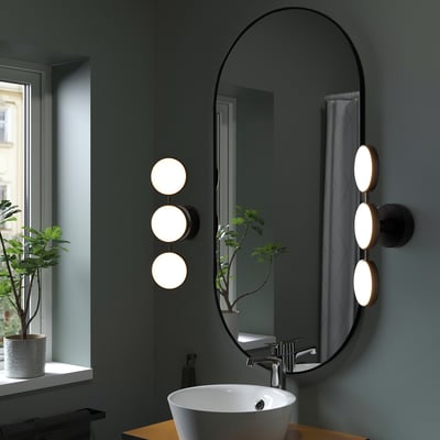 KABOMBA wall lamp: sleek black, oval, with 2 lit circles flanking mirror. Modern-art deco style, aiding bathroom tasks & mood lighting.