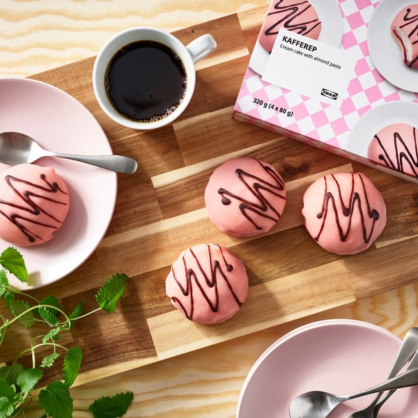 Coffee break kit: frozen pink cream cakes, coffee cup, spoons, on wooden board, with ikea packaging.